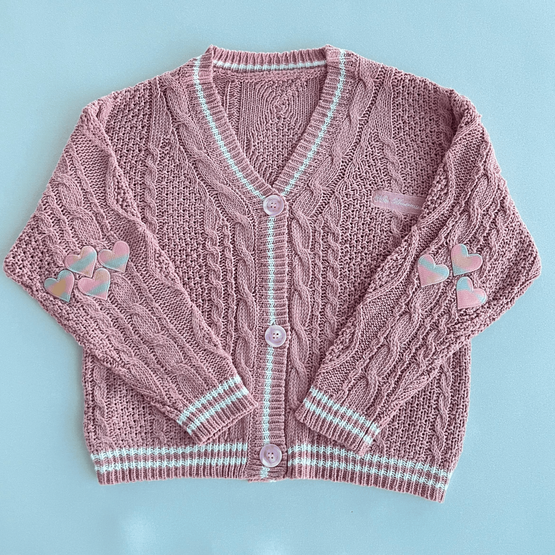 Pink knitted cardigan with heart designs on a light blue background