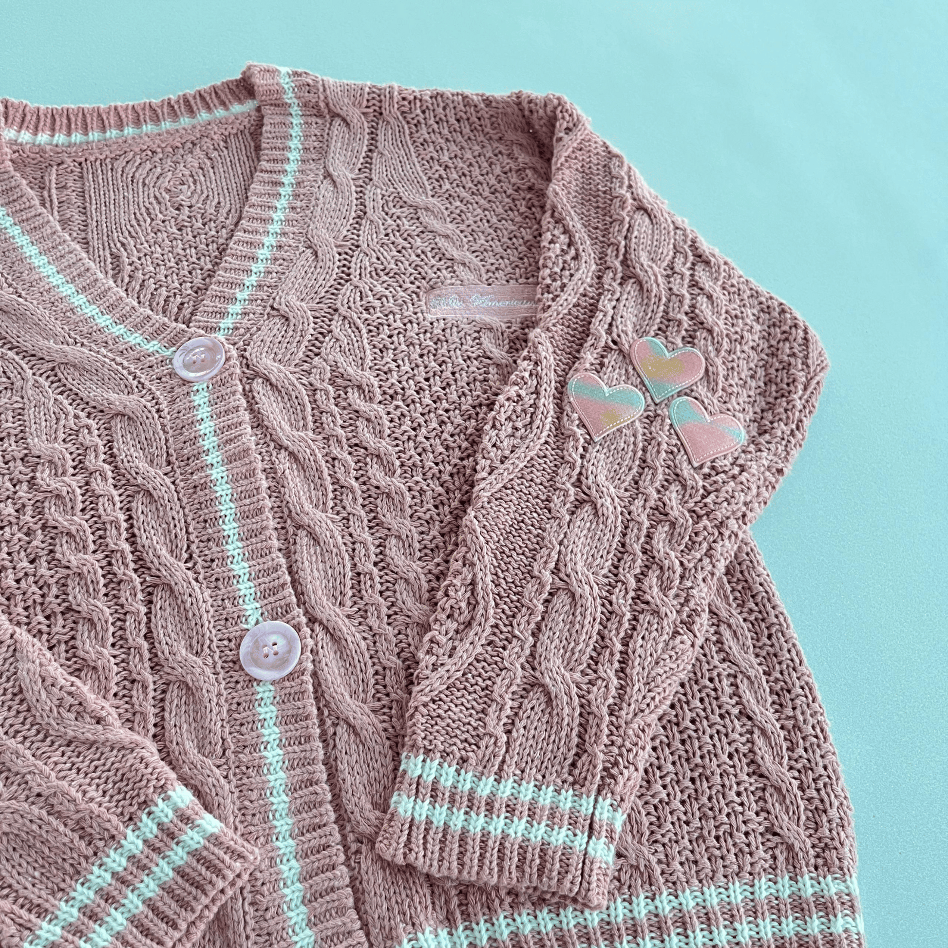 Knitted cardigan with cable pattern and button details on a light blue background