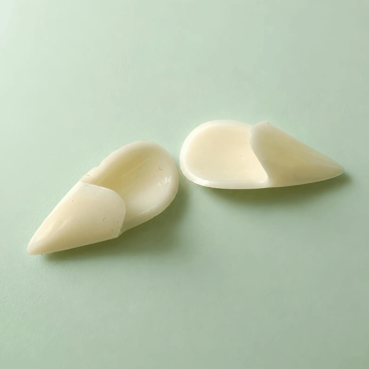 Two off-white silicone or rubber finger tips, likely for massage, therapy, or beauty purposes, displayed on a light mint green background.