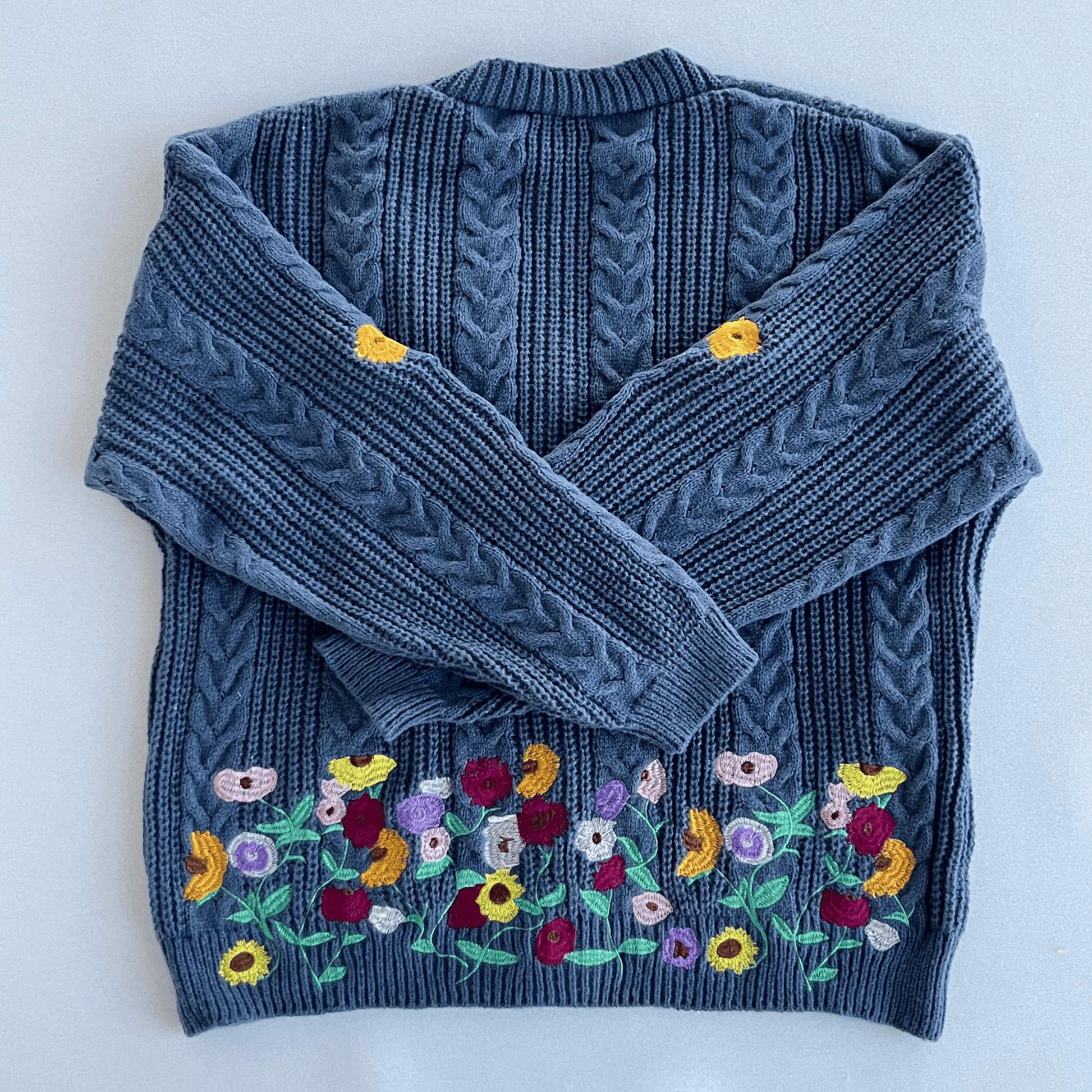 Blue knitted sweater with floral embroidery on a white background