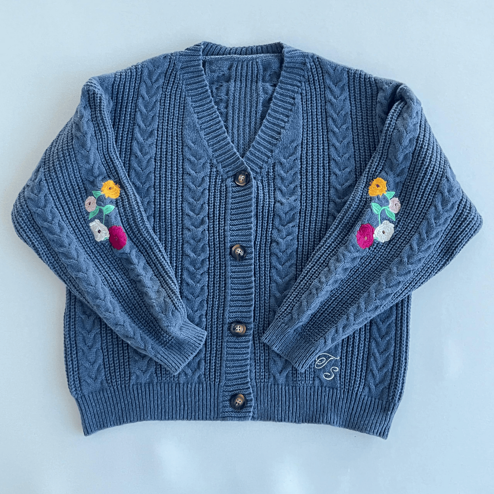 Blue knitted cardigan with floral designs on sleeves against a light blue background