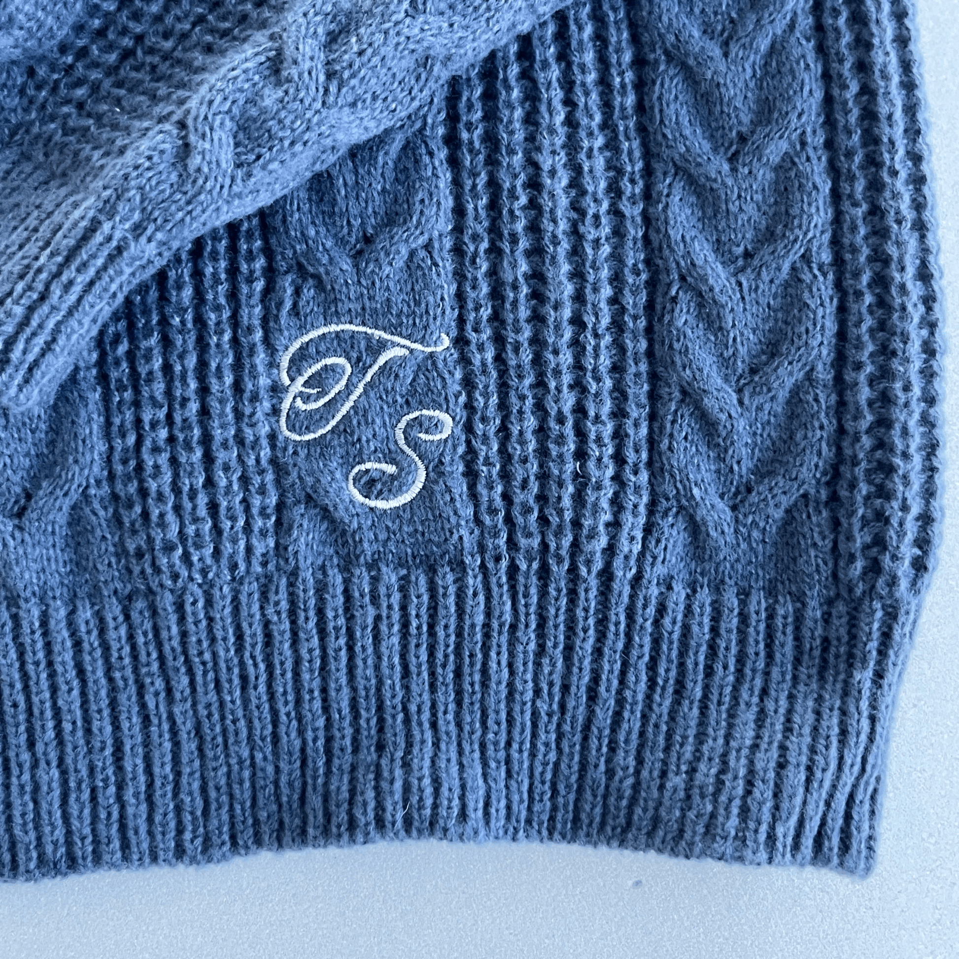 Blue knitted fabric with embroidered initials 'TS' on a white background