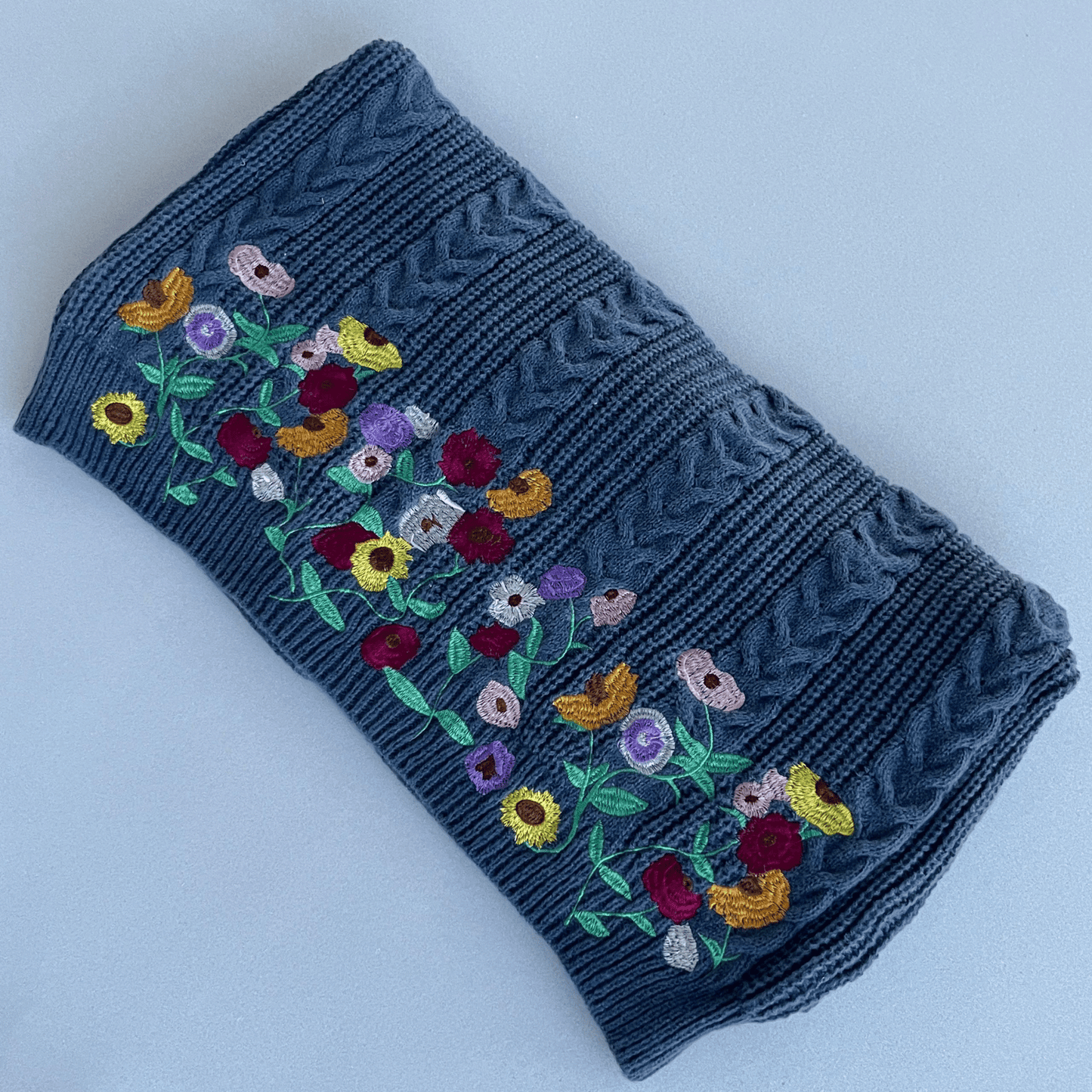 Folded blue knitted fabric with colorful floral embroidery on a light gray background