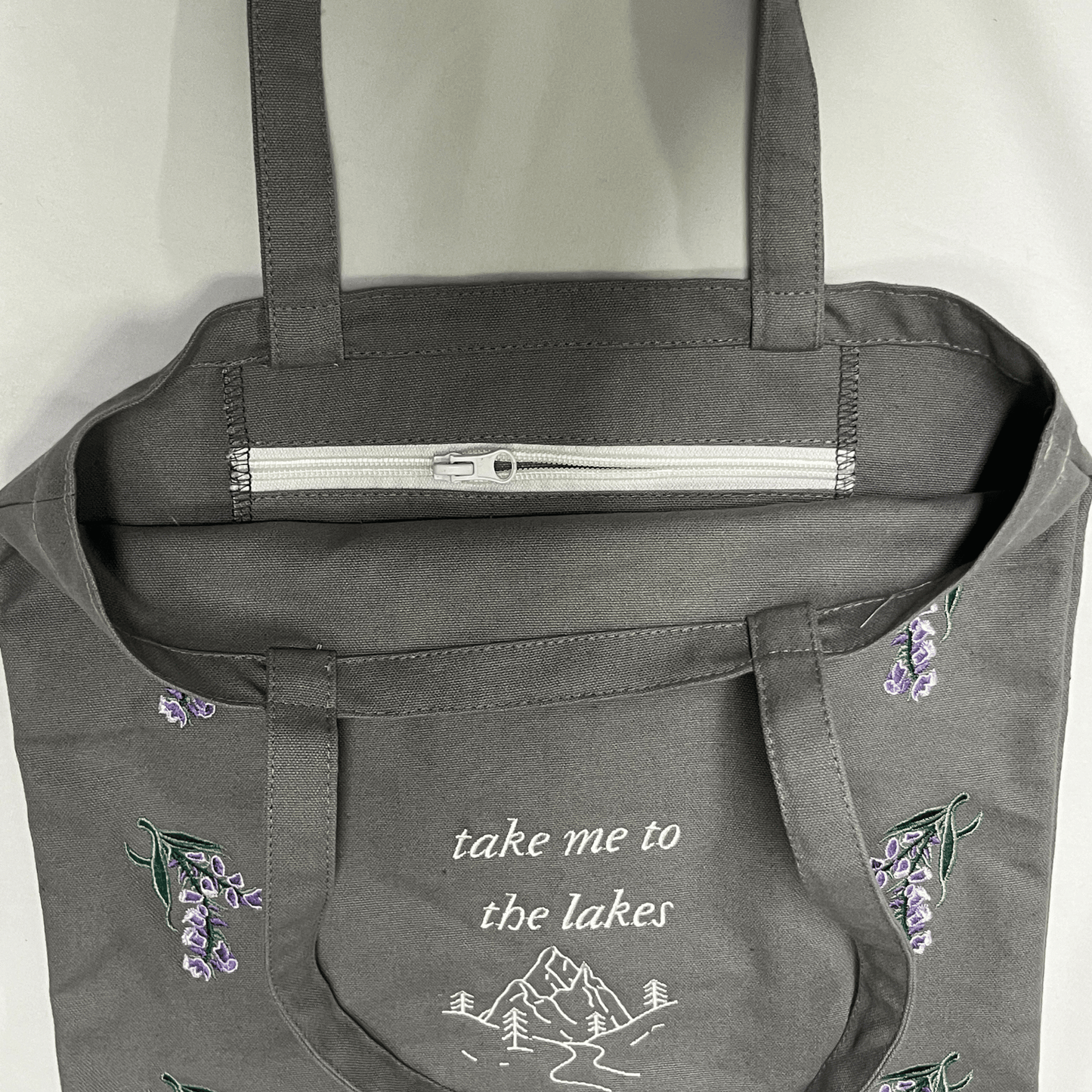 Gray tote bag with floral embroidery and text on a white background