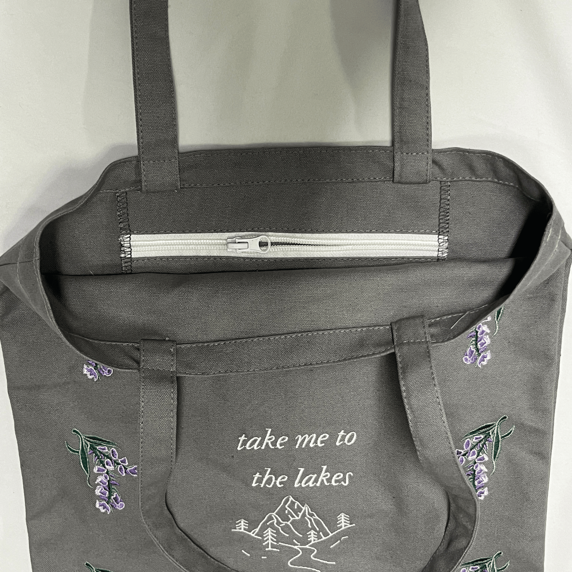 Gray tote bag with floral embroidery and text on a white background
