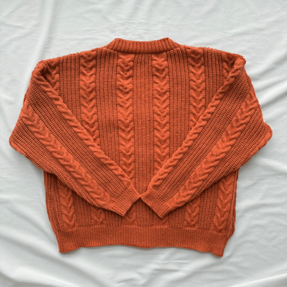 An orange cable-knit sweater laid flat on a white fabric background.