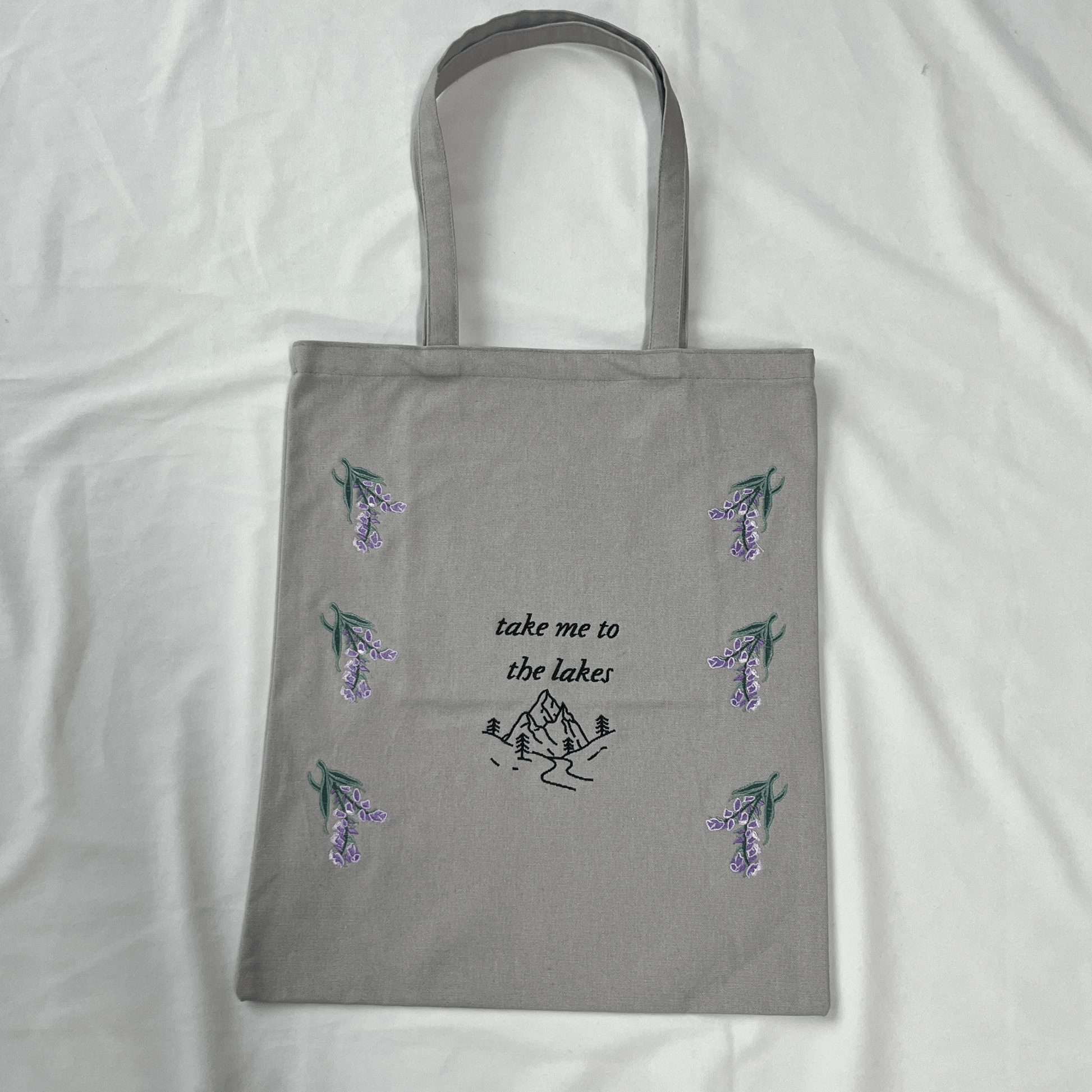 Gray tote bag with floral designs and text on a white background