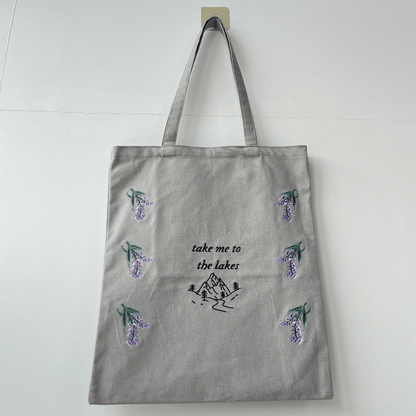 Gray tote bag with nature-themed designs and text on a white background