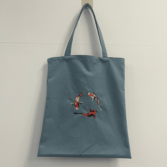 Blue tote bag with fish design on a light gray background