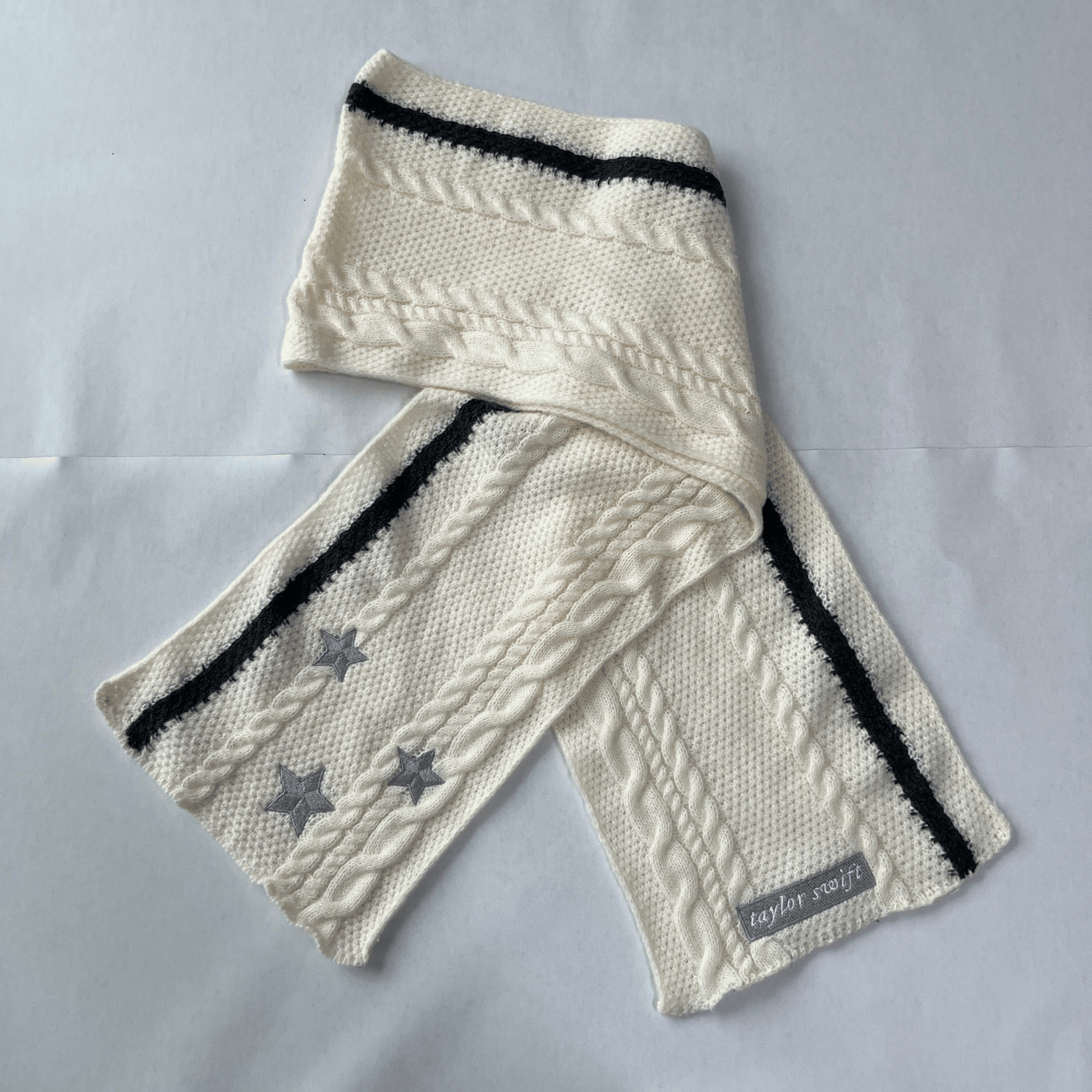 Knitted scarf with star patterns and black stripes on a light gray background