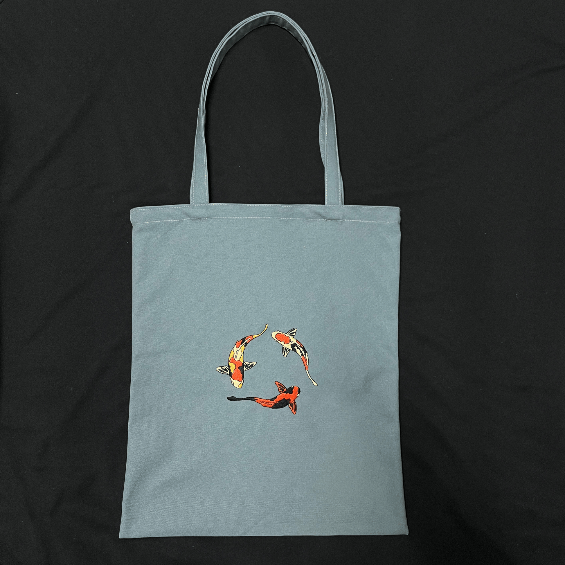 Light blue tote bag with koi fish design on a black background