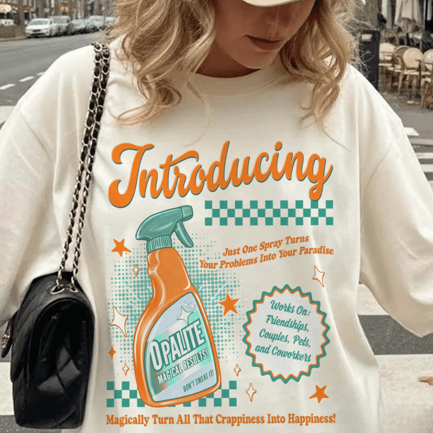 Person wearing a white t-shirt with a colorful graphic and text, standing on a street.