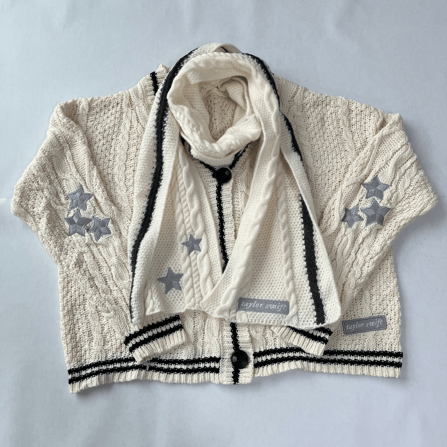 Children's cable knit cardigan with star patterns and a matching scarf on a light gray background.