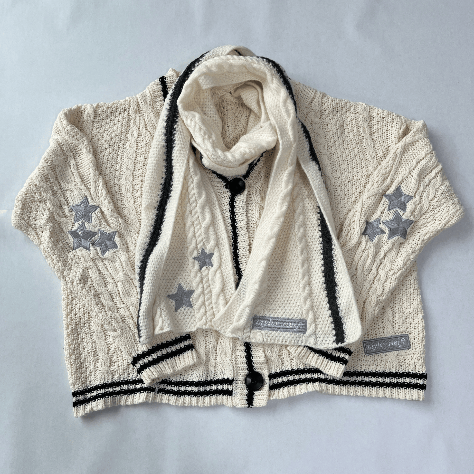 Children's cable knit cardigan with star patterns and a matching scarf on a light gray background.