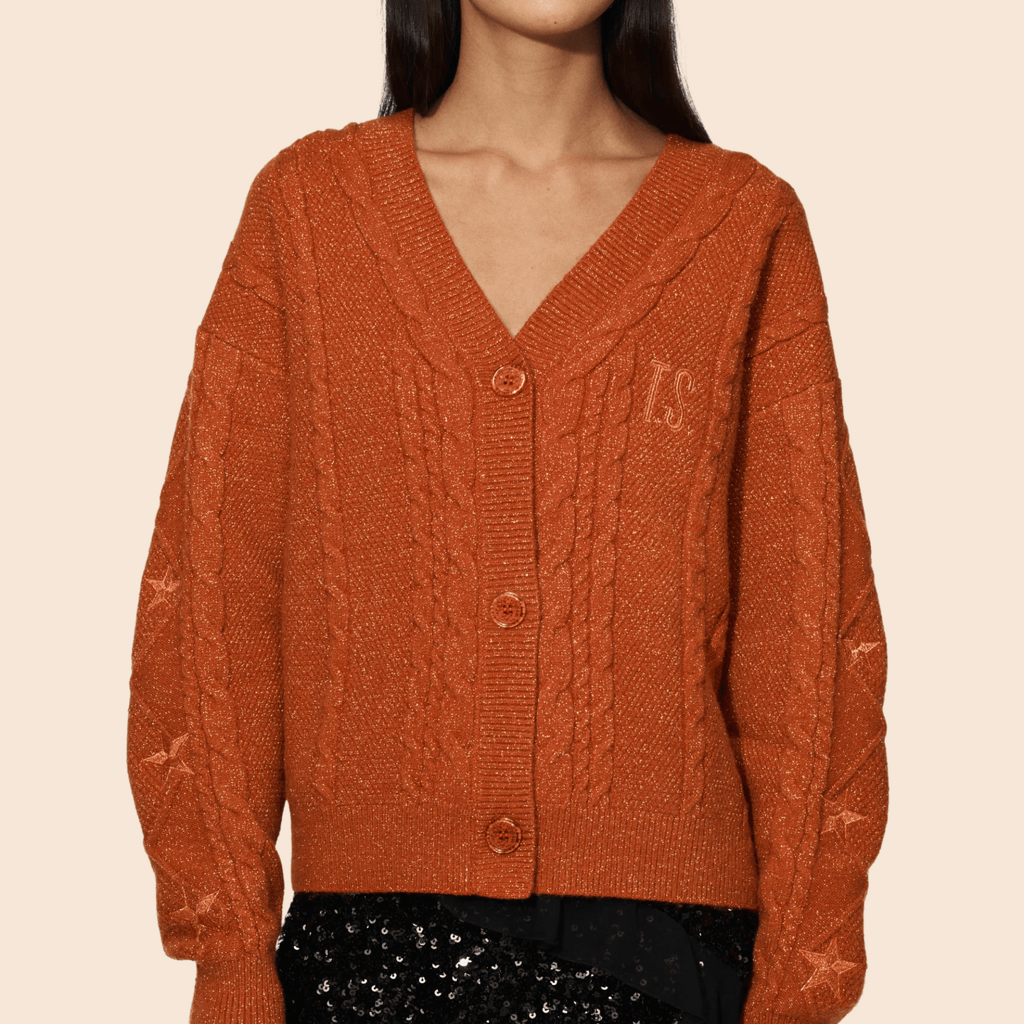 Person wearing a rust-colored cable knit cardigan on a beige background