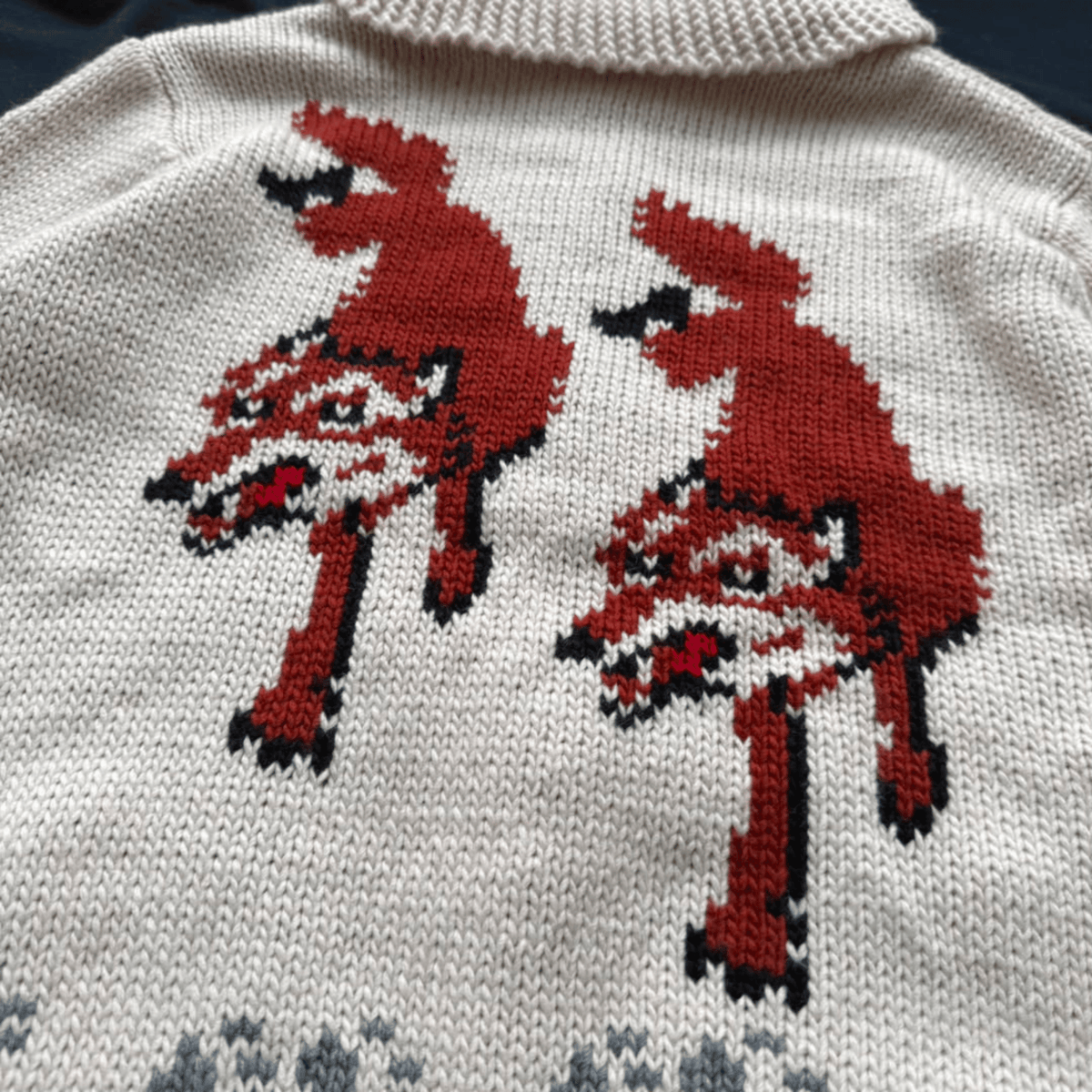 Close-up of a cream knit sweater featuring two large red stylized animal motifs outlined in black across the chest.