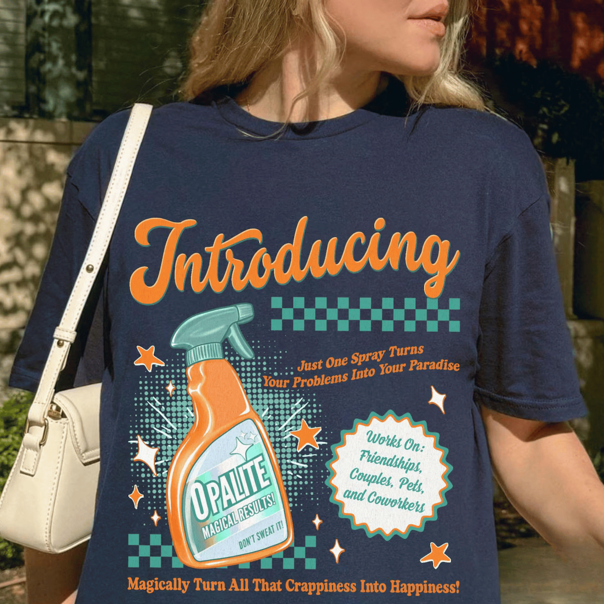 Person wearing a blue t-shirt with a colorful graphic and text, holding a beige handbag.