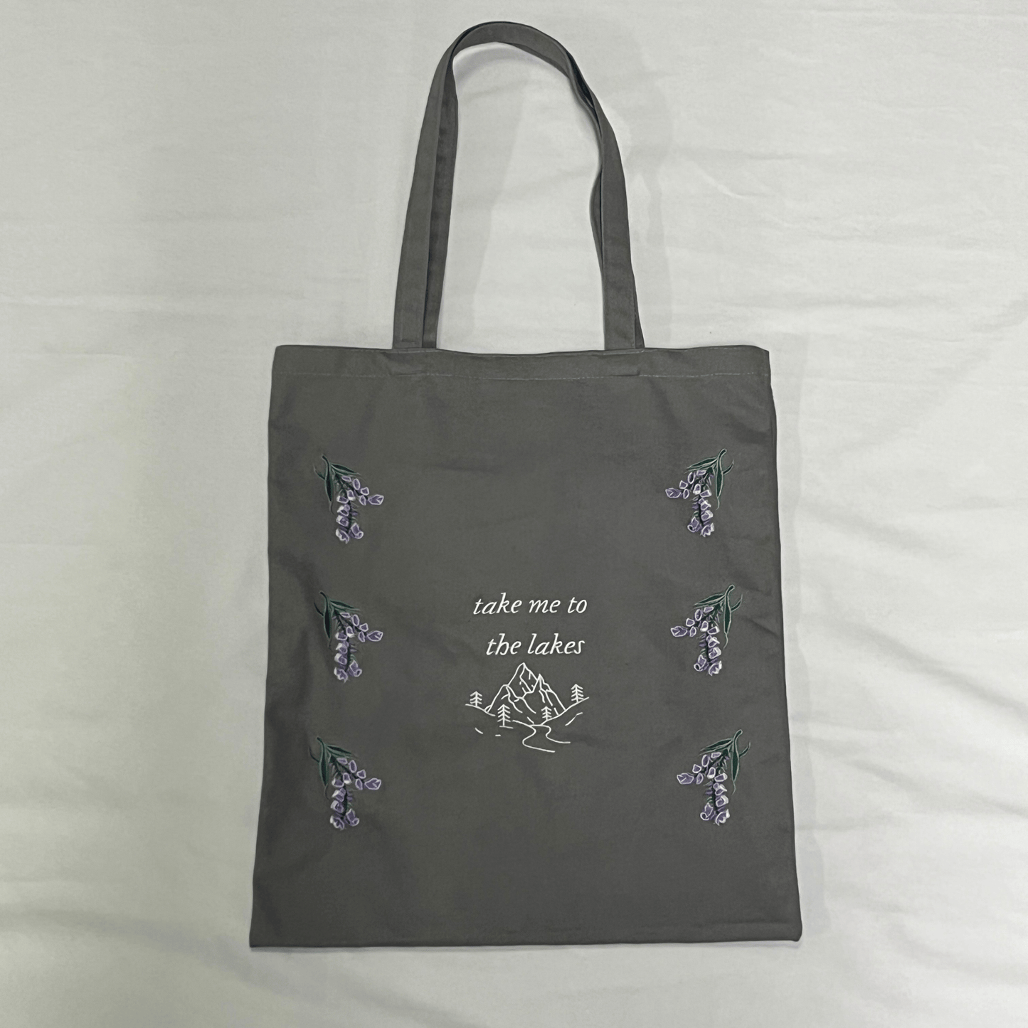 Gray tote bag with nature-themed designs and text on a light gray background