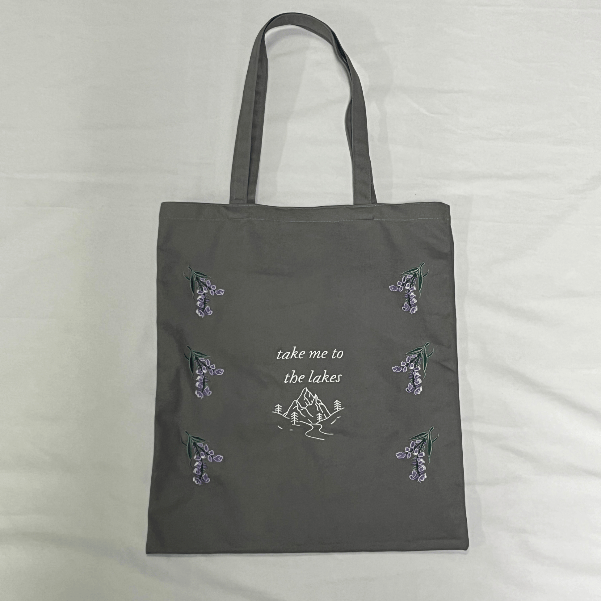 Gray tote bag with nature-themed designs and text on a light gray background