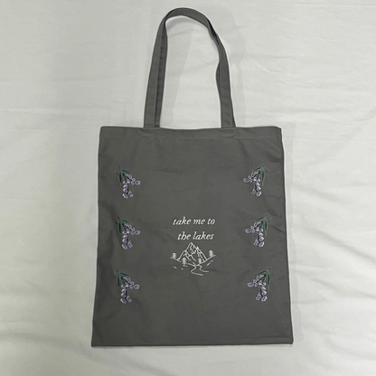 Gray tote bag with nature-themed designs and text on a light gray background
