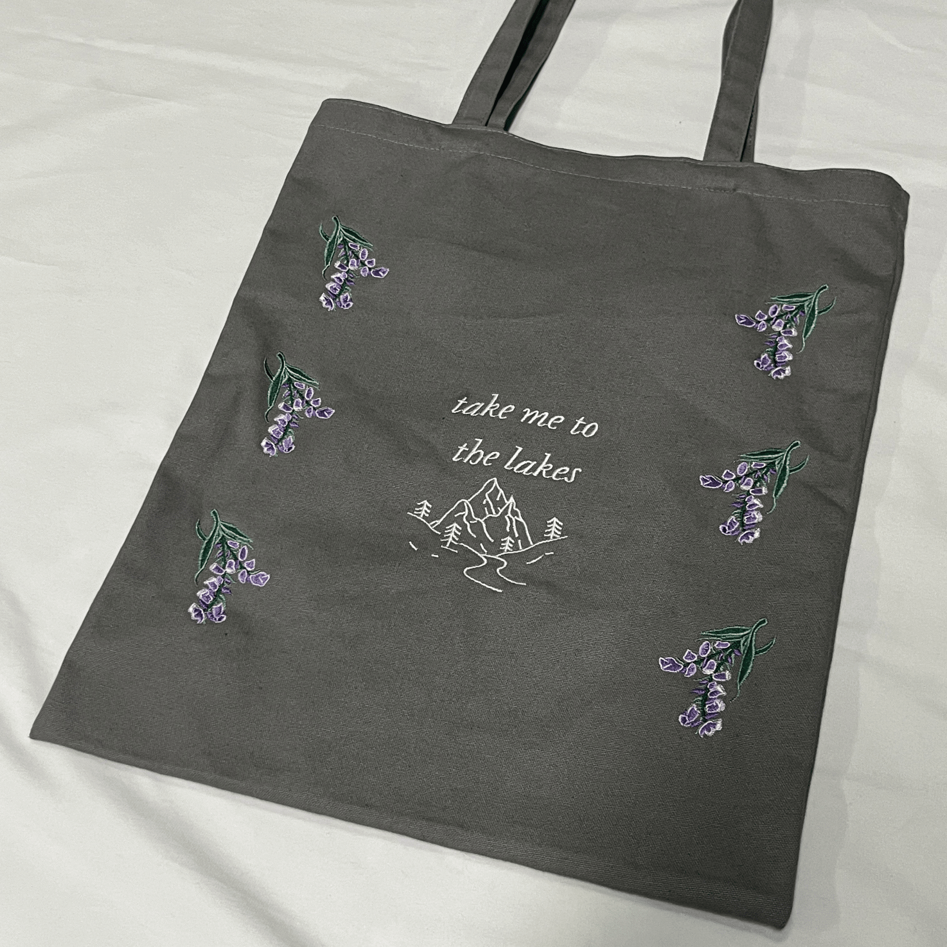 Gray tote bag with embroidered designs and text on a white background