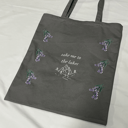 Gray tote bag with embroidered designs and text on a white background