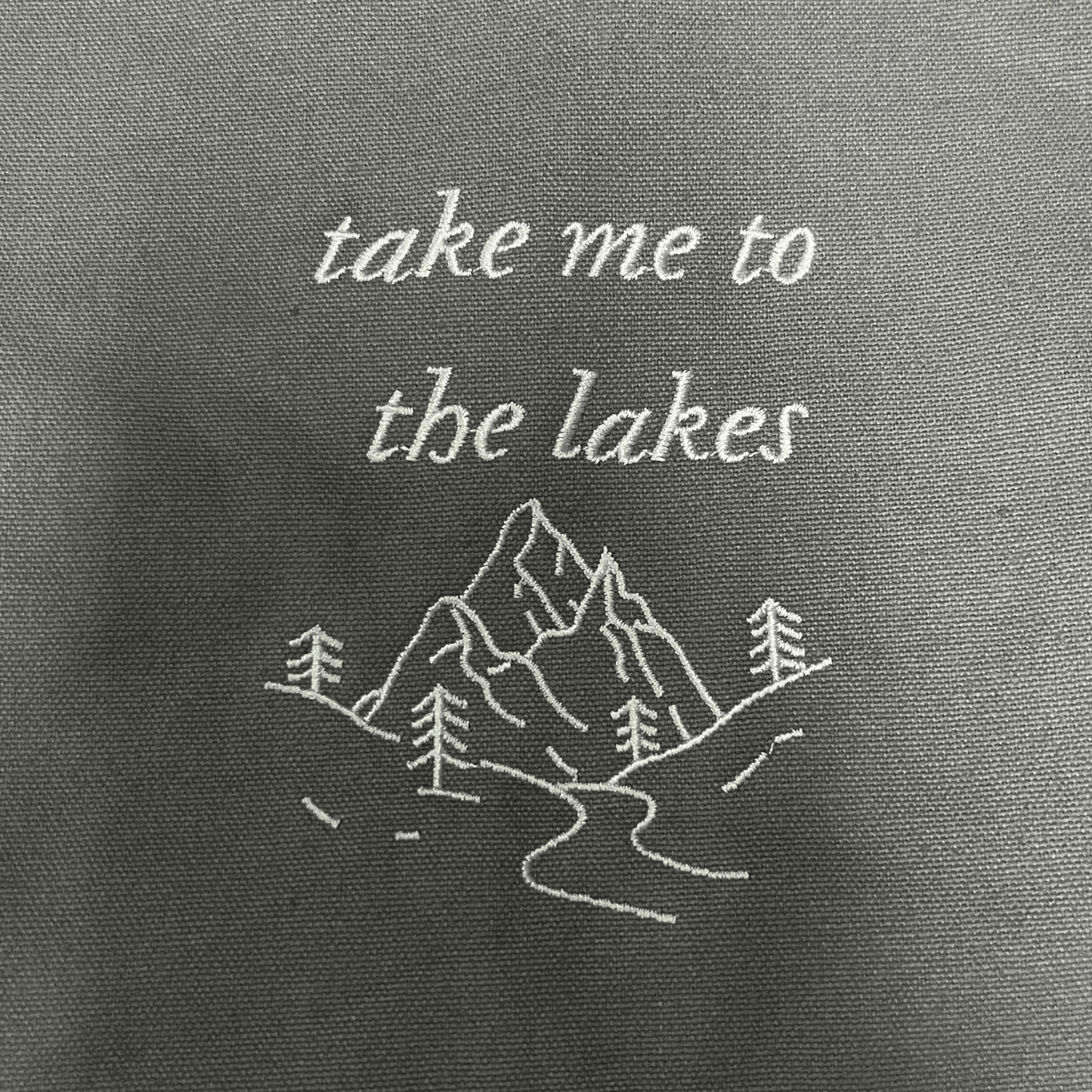 Embroidered text and mountain design on a gray fabric background