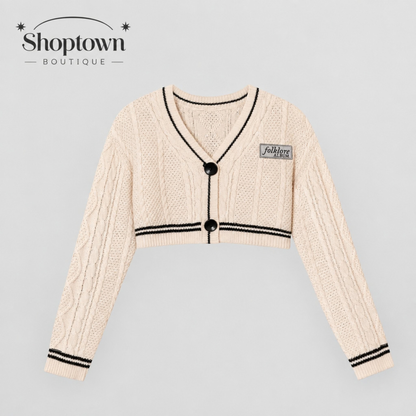 A cream-colored folklore knit cardigan sweater with black trim, black buttons, and a small 'fashionable' patch on the chest, displayed against a light gray background with the 'Shoptown Boutique' logo in the top left corner.