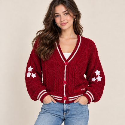 A woman wearing a red cable-knit cardigan with white trim and white star details on the sleeves, paired with light blue jeans, against a solid beige background.