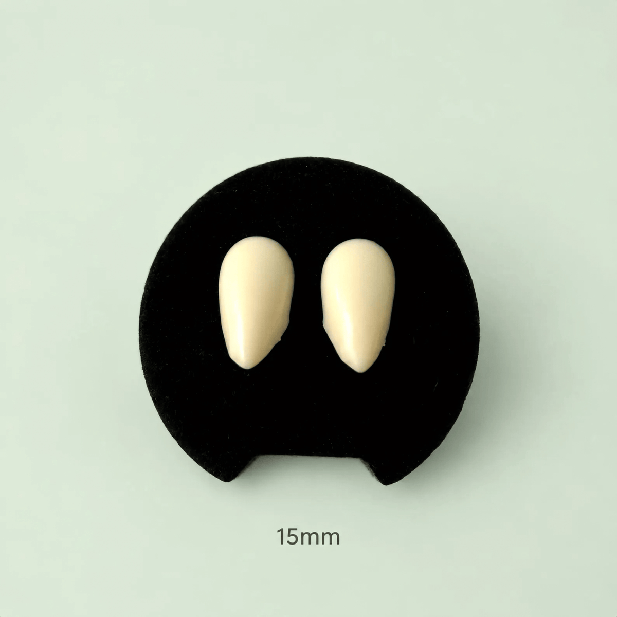 Two small oval cream-colored dental impression material pieces displayed on a black circular stand against a pale mint background, with '15mm' text below.