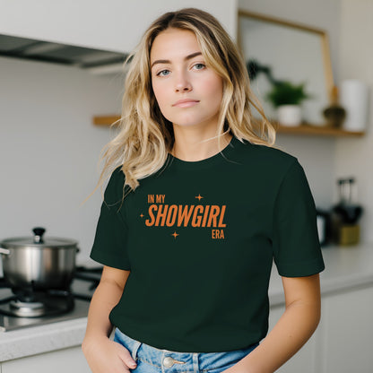 Woman wearing a dark green t-shirt with 'In My Showgirl Era' text in a kitchen.