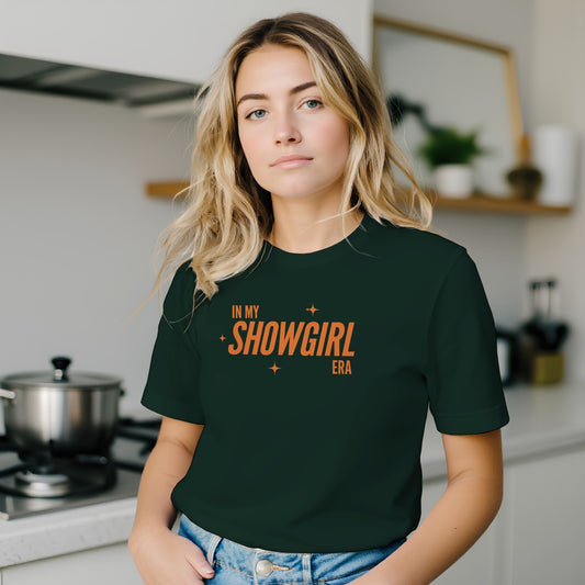 Woman wearing a dark green t-shirt with 'In My Showgirl Era' text in a kitchen.