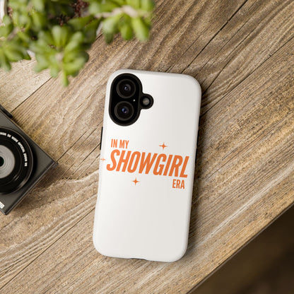 Phone case with 'In My Showgirl Era' text on a wooden surface with a camera and plant.