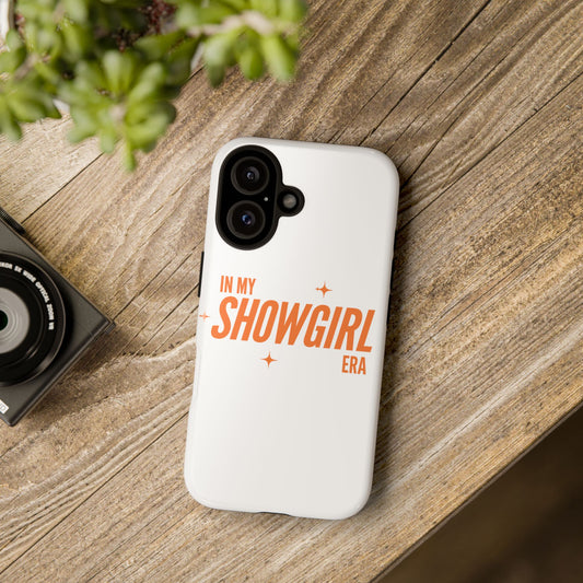 Phone case with 'In My Showgirl Era' text on a wooden surface with a camera and plant.