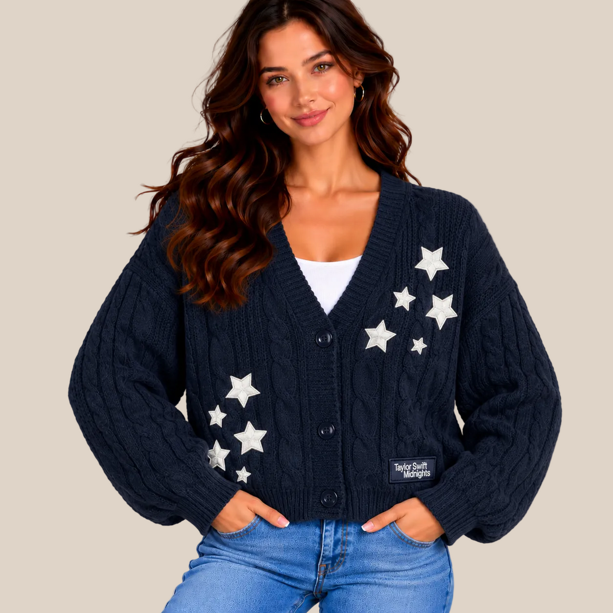 A woman wearing a navy blue cable-knit cardigan with white embroidered stars, styled with a white top and blue jeans against a warm beige background.