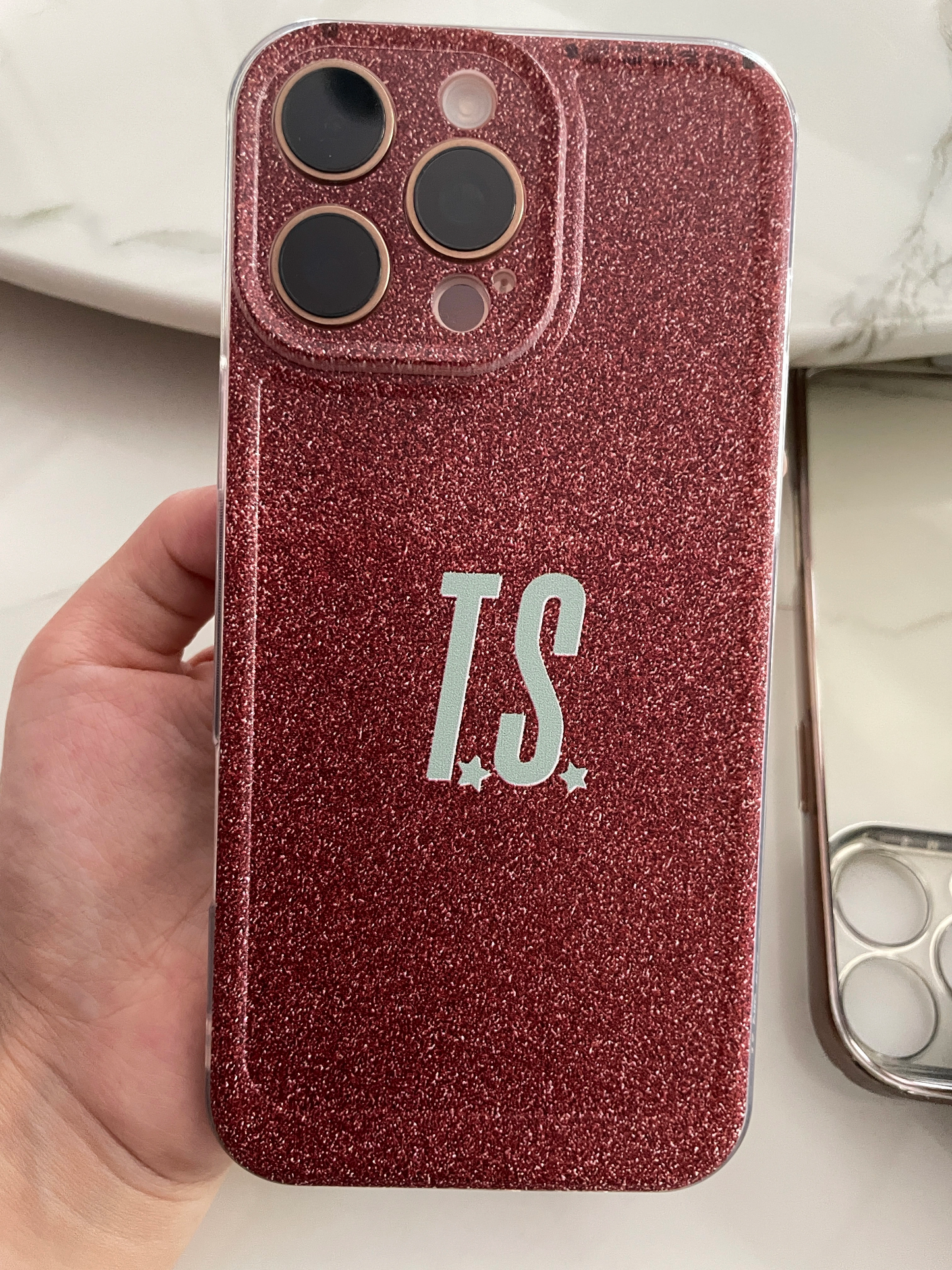 Phone case with 'T.S.' initials held by a hand on a light background