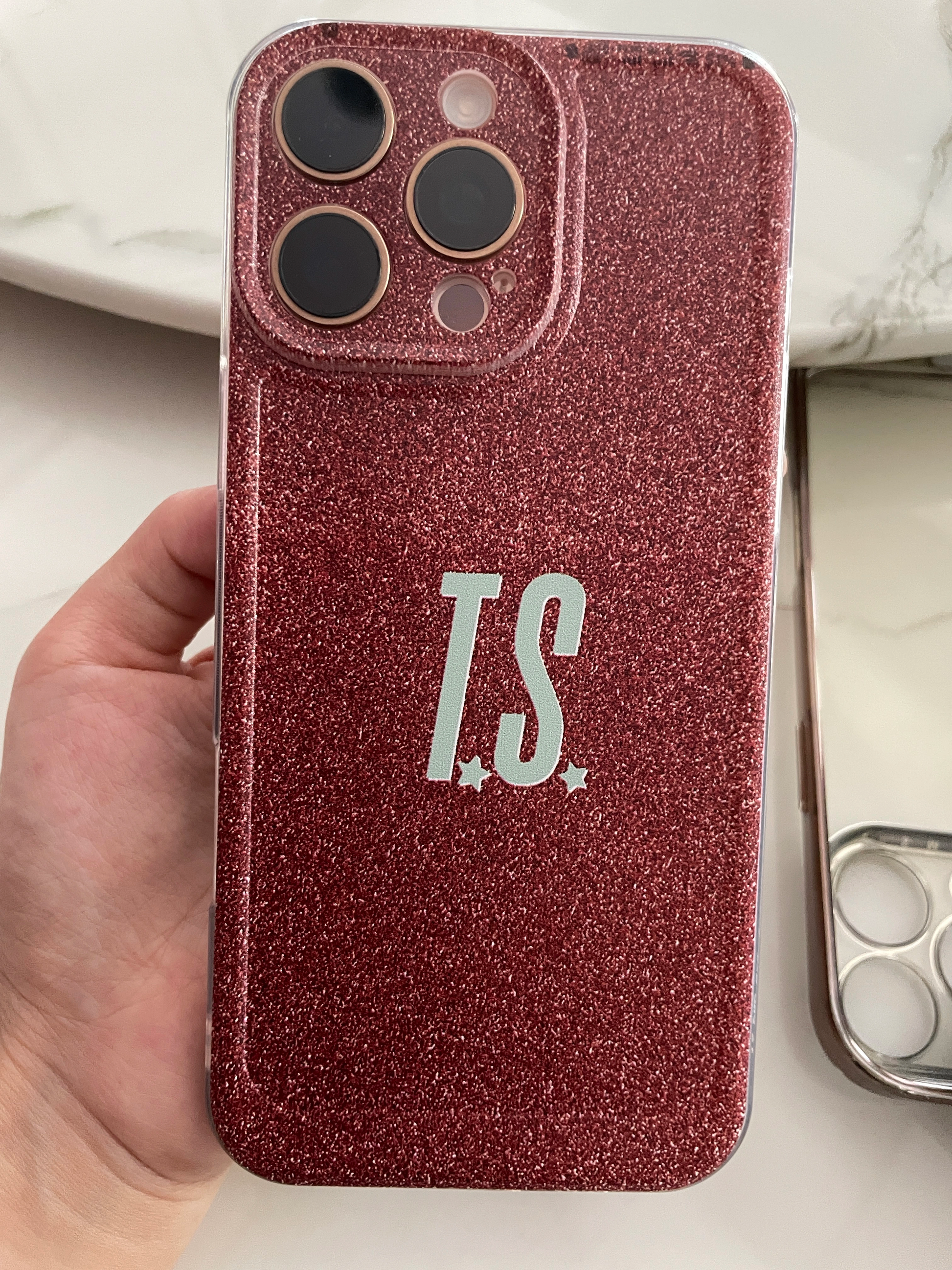 Phone case with 'T.S.' initials held by a hand on a light background