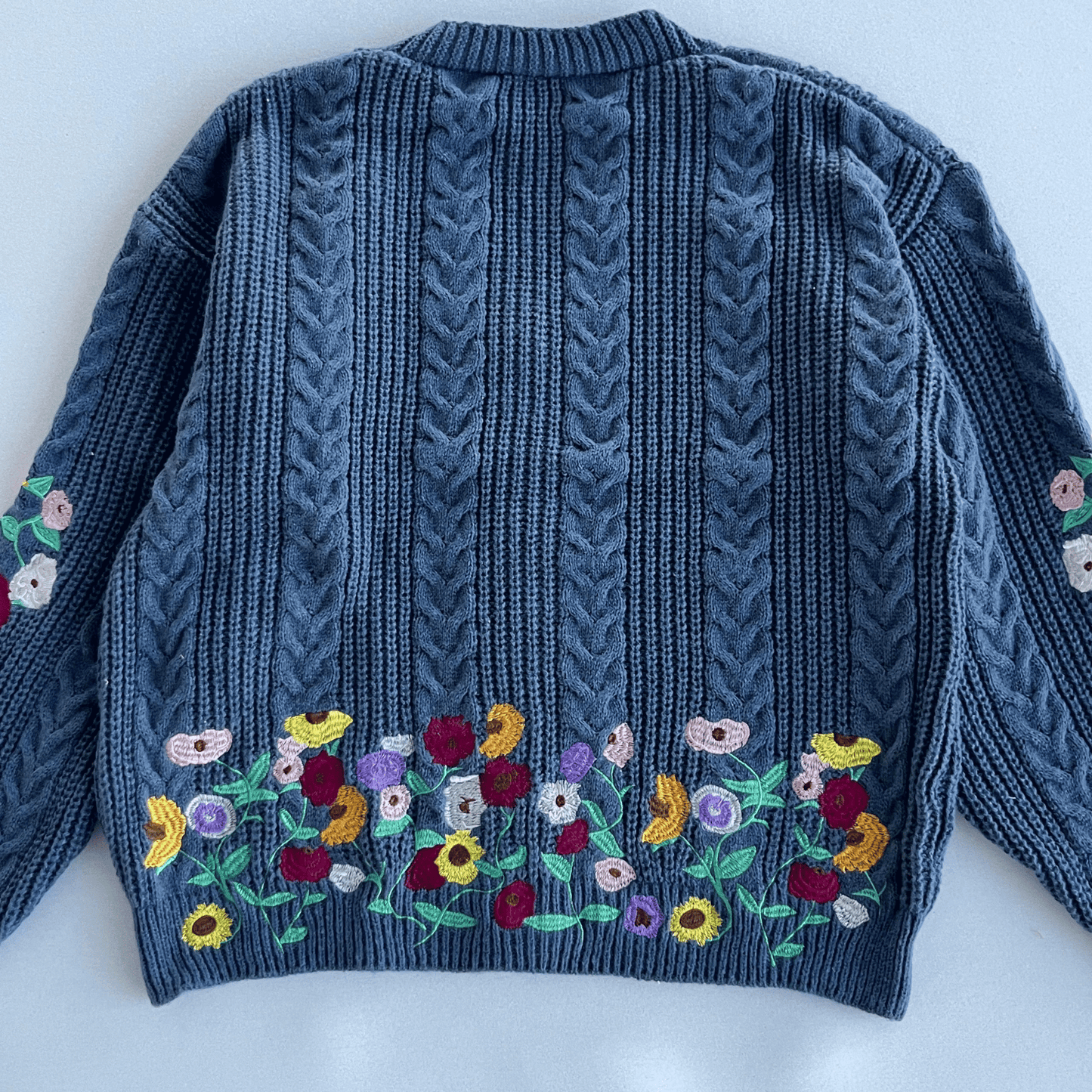 Blue knitted sweater with floral embroidery on a white background