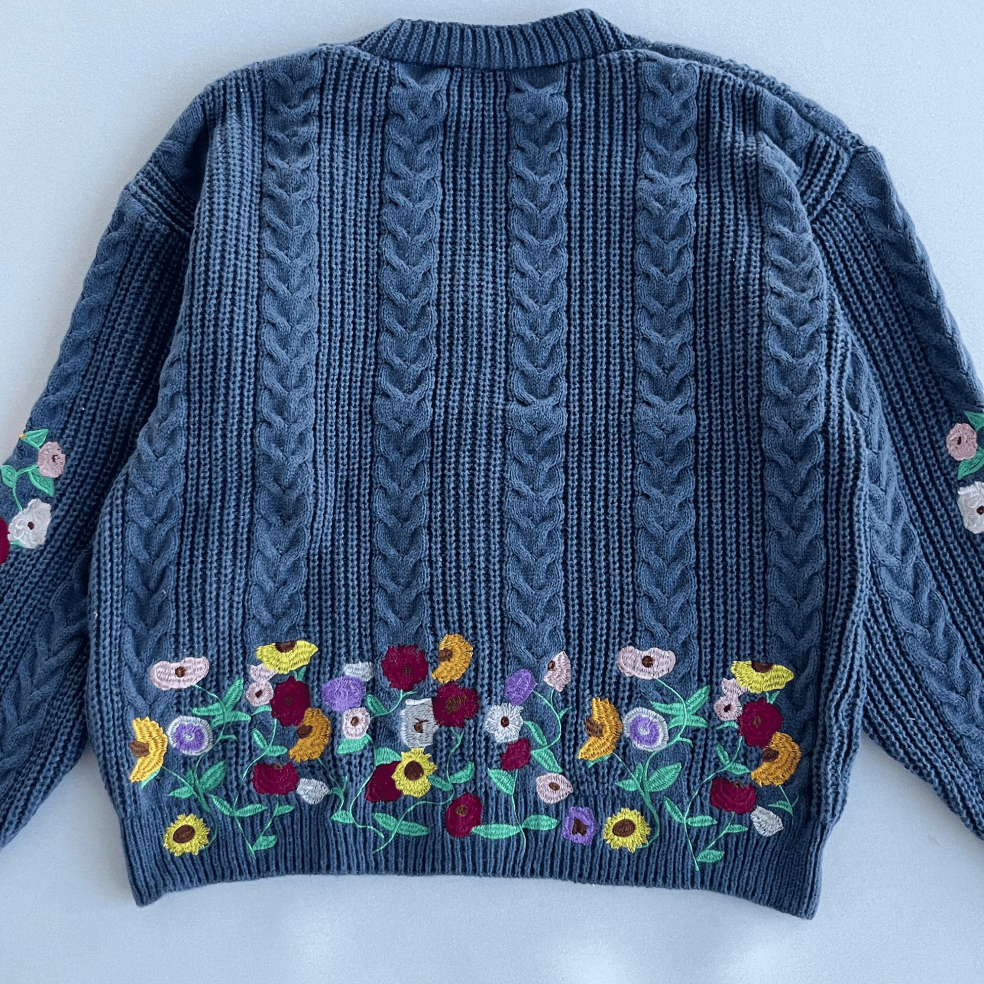 Blue knitted sweater with floral embroidery on a white background