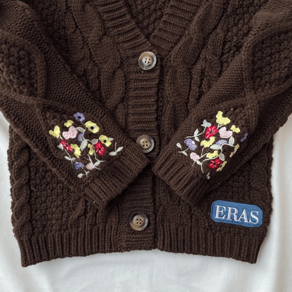 Brown cable knit cardigan with floral embroidery on sleeves and 'ERAS' logo on a white background
