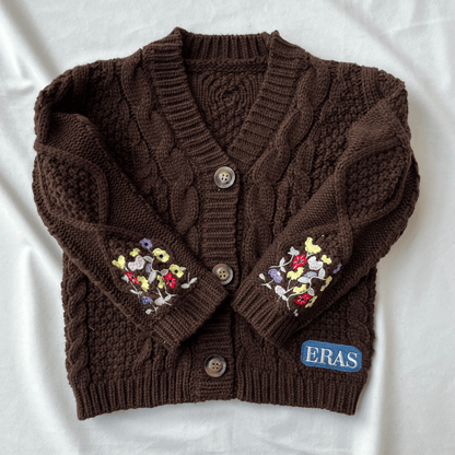 Brown knitted cardigan with floral embroidery on sleeves and 'ERAS' brand label, on a white background