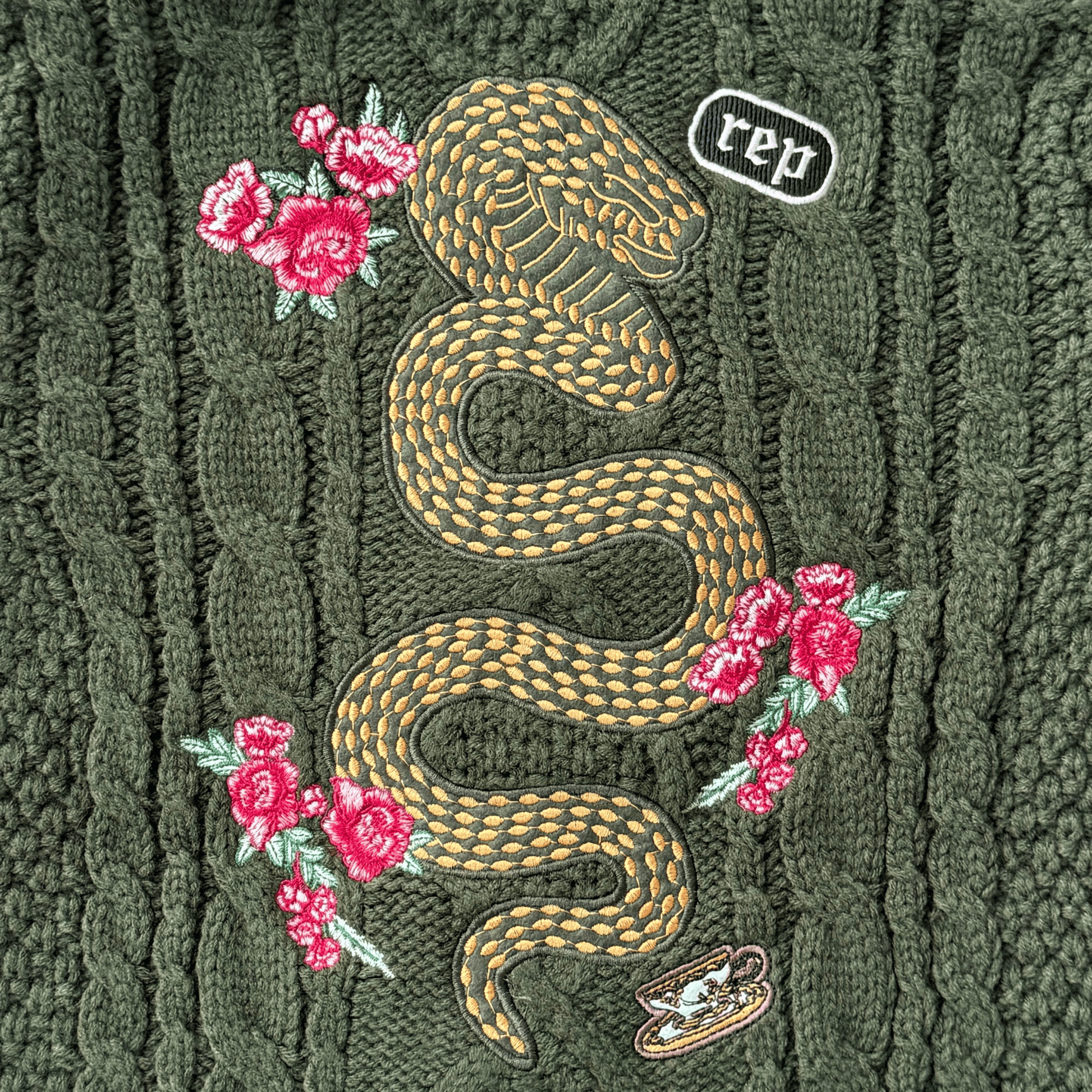 Embroidered snake design on a textured green fabric with pink flowers.