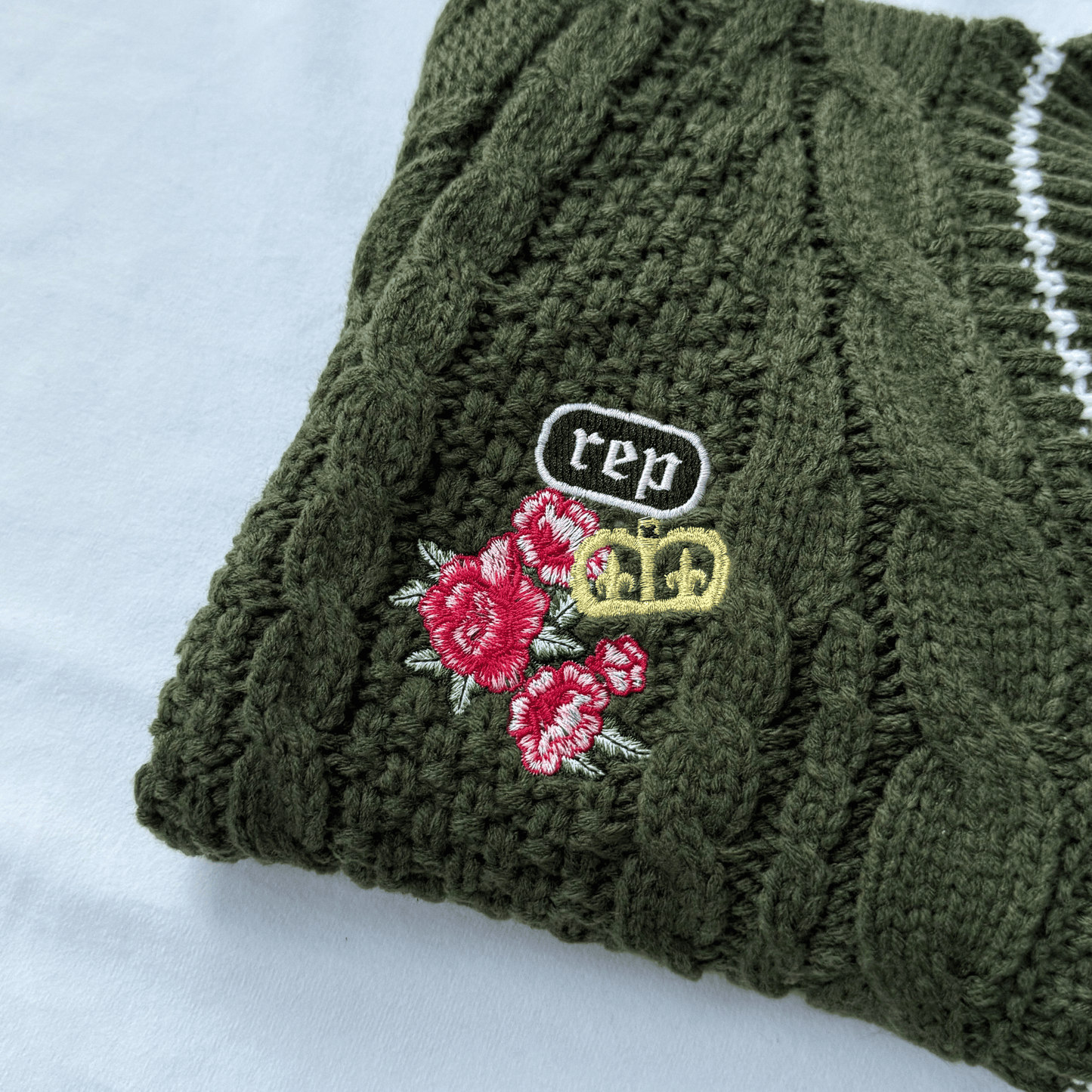 Green knitted sweater with floral and 'rep' embroidery on a white background