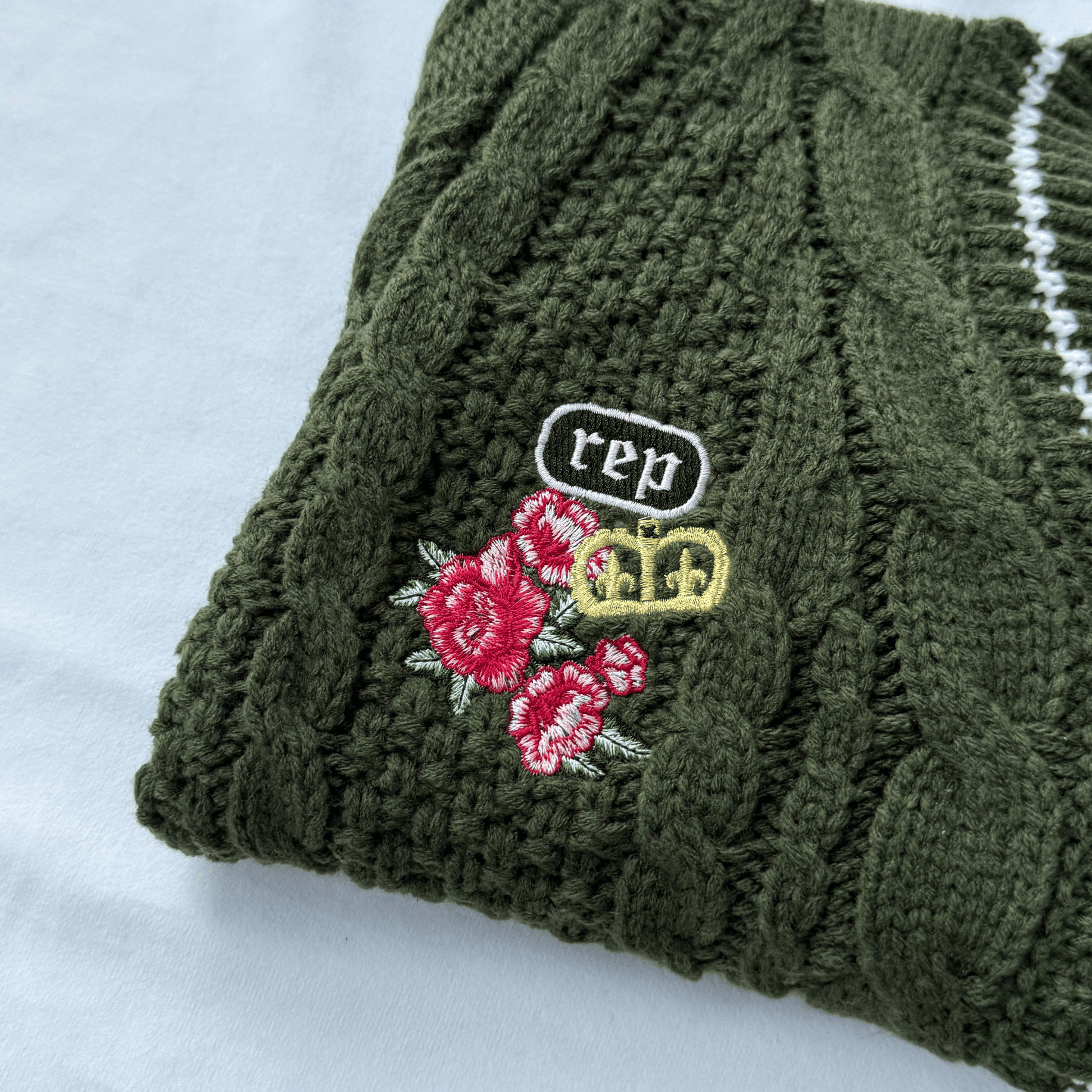 Green knitted sweater with floral and 'rep' embroidery on a white background