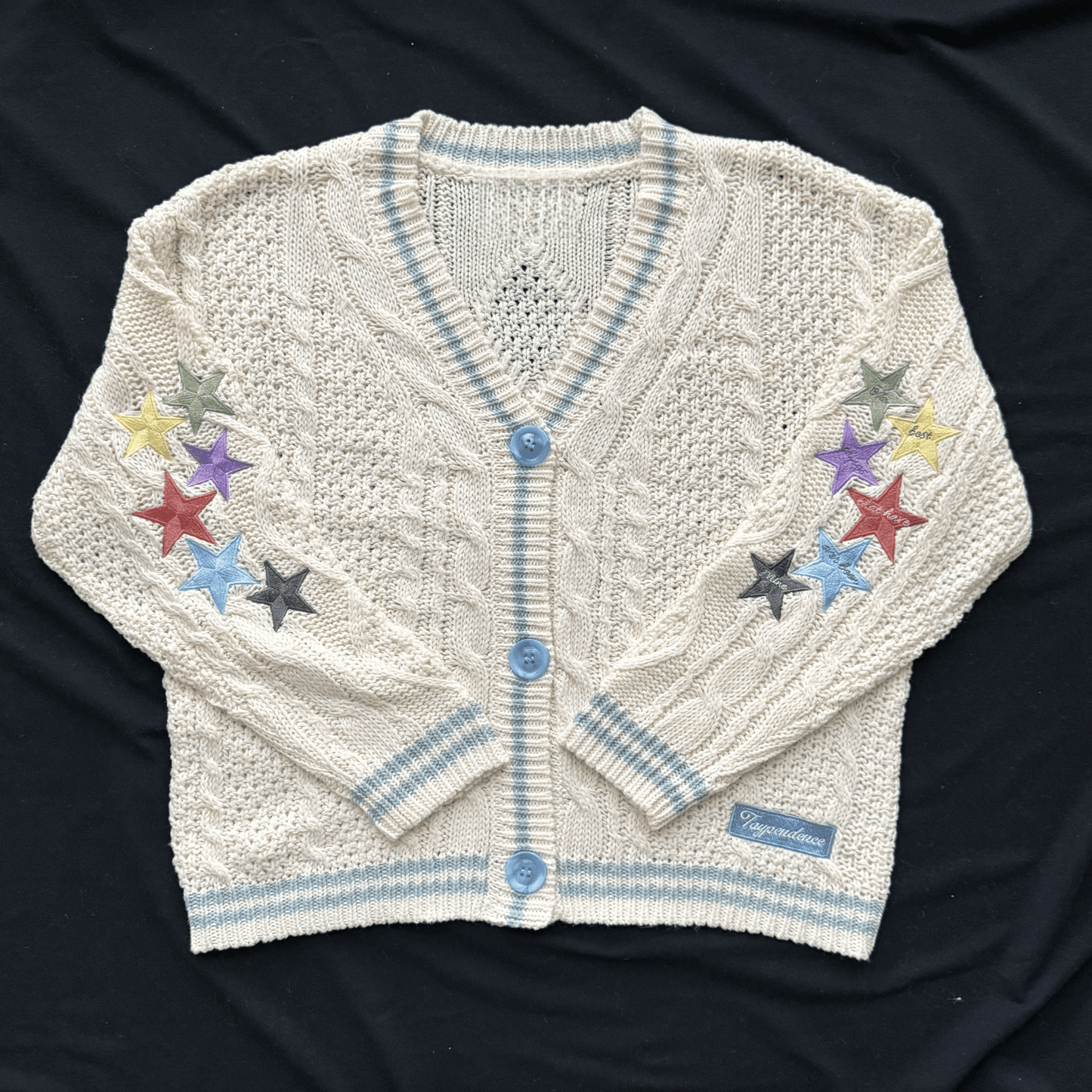 White knitted cardigan with colorful star designs on a dark background