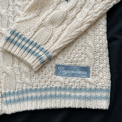 Close-up of a cream knitted sweater with blue stripes and a brand label on a dark background