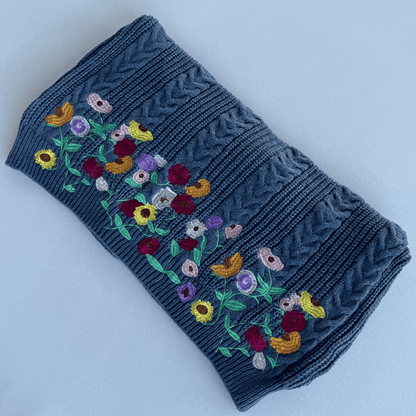 Folded blue knitted fabric with colorful floral embroidery on a light gray background