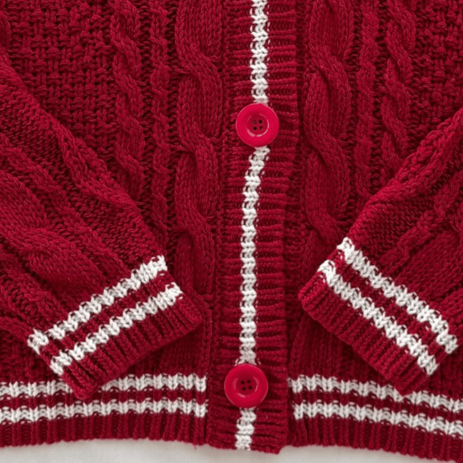 A close-up of a red cable-knit cardigan sweater with white striped accents on the cuffs and hem, and two red buttons down the front.