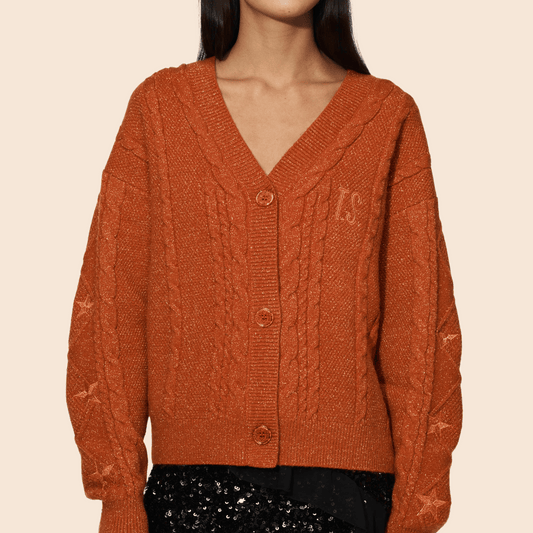 Person wearing a rust-colored cable knit cardigan on a beige background