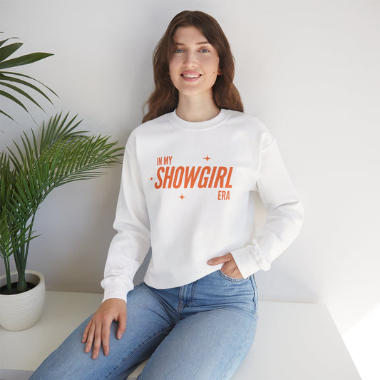 Woman wearing a white sweatshirt with 'In My Showgirl Era' text, sitting in a room with a plant.